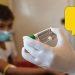 Medical Worker in a Mask and Gloves Holding Vaccine Vials, with a Yellow Warning Bubble in the Corner. - Enbroncados