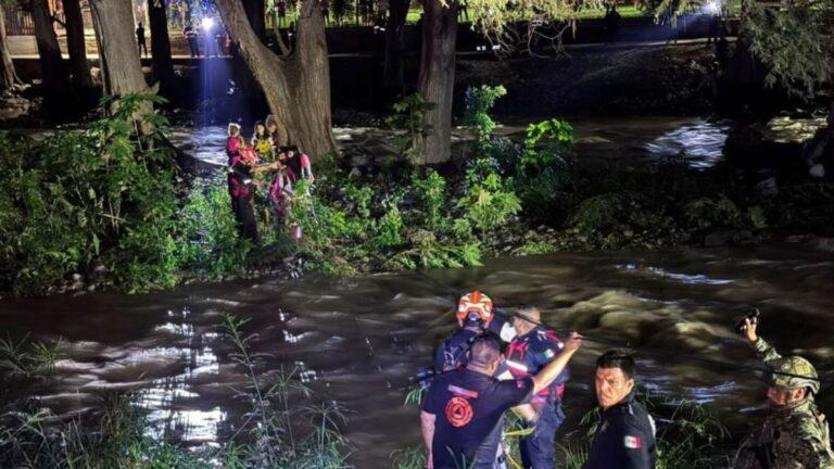 Emergency Responders in Gear Help a Person from a River at Night, with Others on the Riverbank Observing and a Tree-lined Backdrop. - Enbroncados