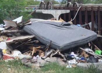 Pile of trash and a large discarded mattress wedged under a bridge or overpass.