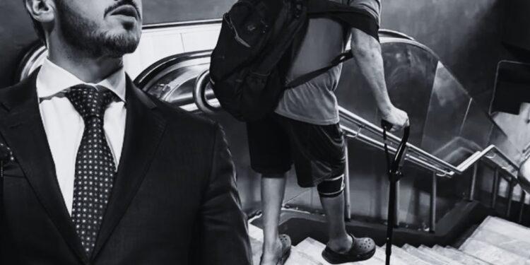 Peligro-en-las-escaleras-del-metro-de-nuevo-leon - Enbroncados in Grayscale, a Man in a Suit Stands at the Left While Another Person with a Backpack and a Crutch Climbs Down a Stairwell Behind Him. - Enbroncados