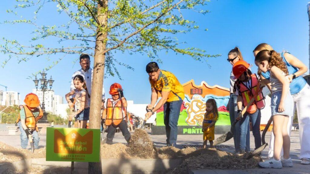 Arboles-un-millon-oms - Enbroncados Group of Volunteers and Children Planting a Tree at a Community Event, with a Colorful Mural in the Background. - Enbroncados