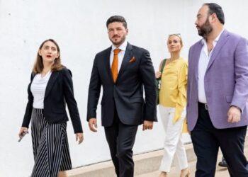 Samuel García Viste Traje Negro Con Corbata Naranja Mientras Camina Al Aire Libre Junto a Colaboradores Y Funcionarios - Enbroncados