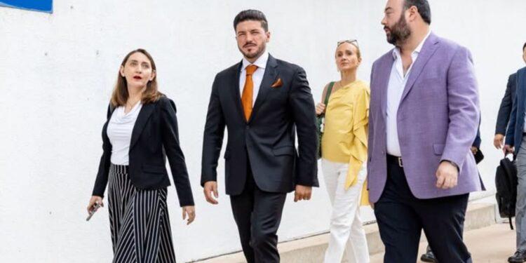Samuel García Viste Traje Negro Con Corbata Naranja Mientras Camina Al Aire Libre Junto a Colaboradores Y Funcionarios - Enbroncados
