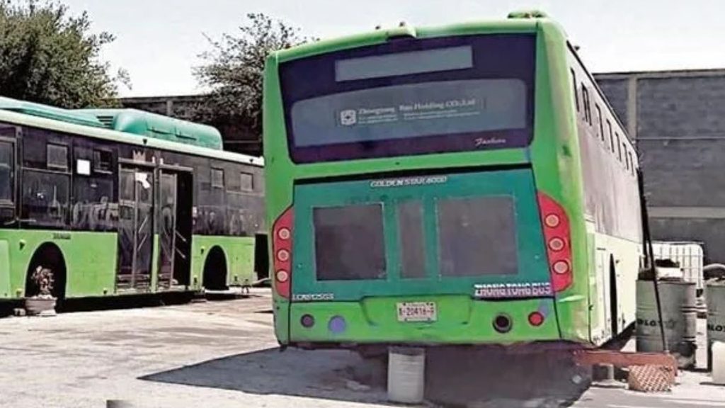 Rear View of a Bright Green City Bus Raised on a Concrete Block in a Bus Depot, Another Bus in Background. - Enbroncados