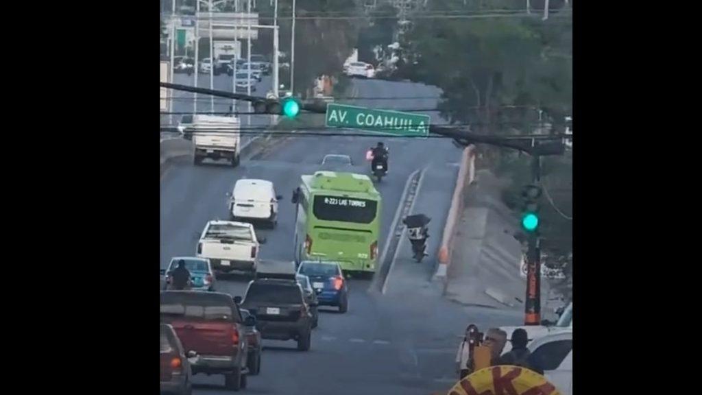 Urban Street Scene with a Green Bus in the Middle Lane, Several Cars, a Motorcycle, and Pedestrians Near a Traffic Light. - Enbroncados