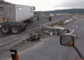 Semi-trailer Obstructing a Curved Highway with Scattered Debris and Damaged Guardrails; Two People Assess the Scene, with a Truck Side Mirror Visible in the Foreground. - Enbroncados